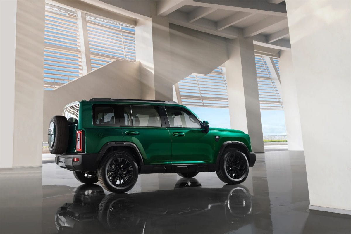 Side profile of green Haval V7 SUV with black alloy wheels and roof rack in a modern urban setting.